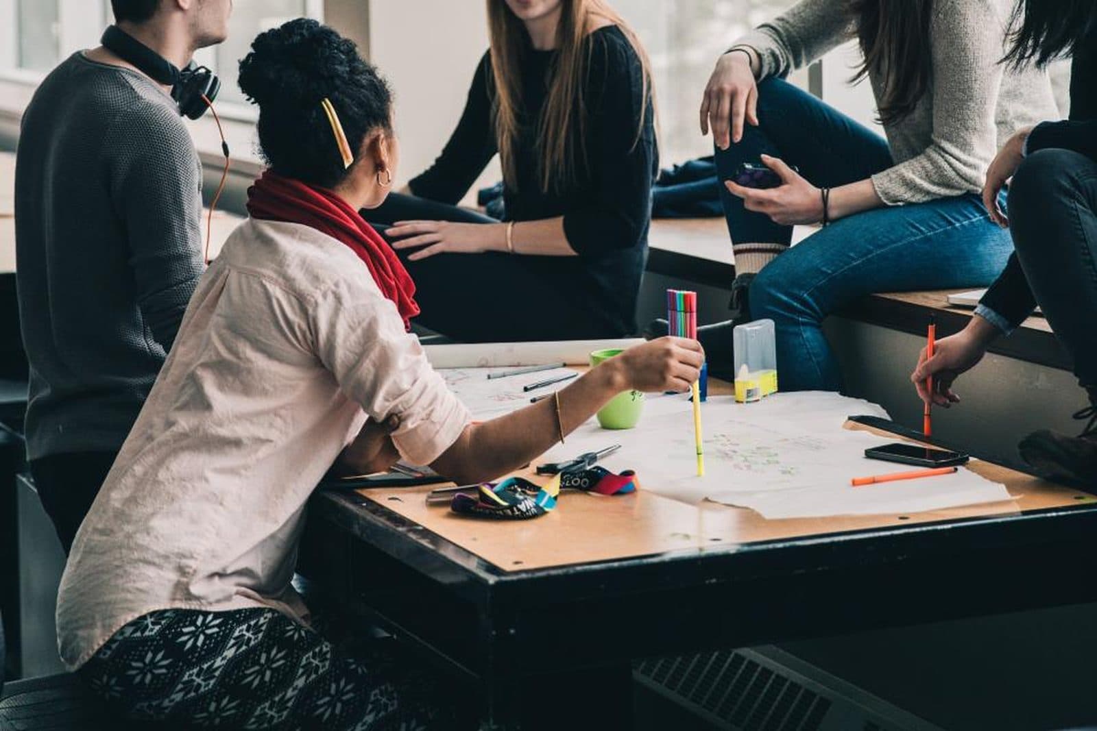 Un groupe d'étudiants travaille ensemble autour d'une table, feutres et feuilles en main
