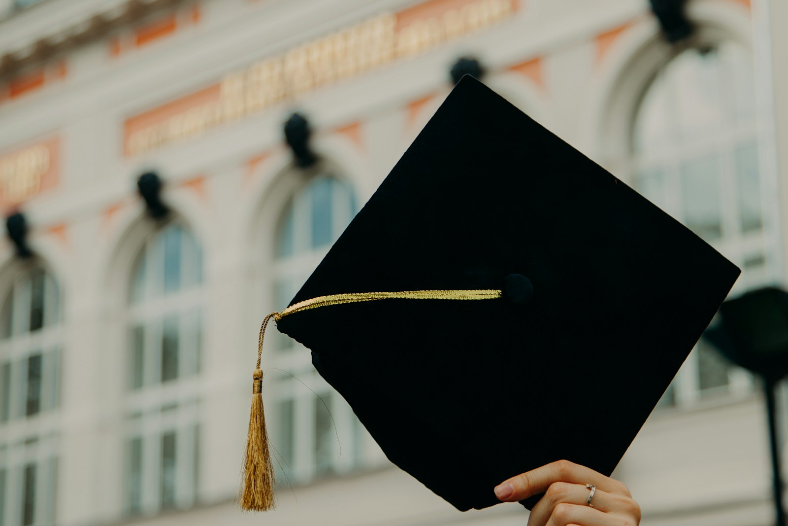 Une main tenant une toque de diplômé devant un bâtiment universitaire